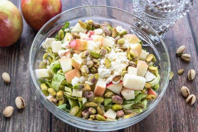Brussels sprouts apple salad in a glass serving bowl topped with feta cheese.