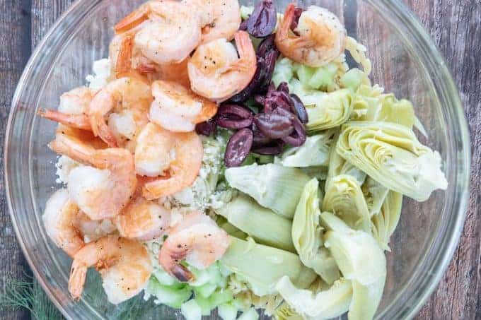 A dish is filled with shrimp, olives, cucumber and artichokes