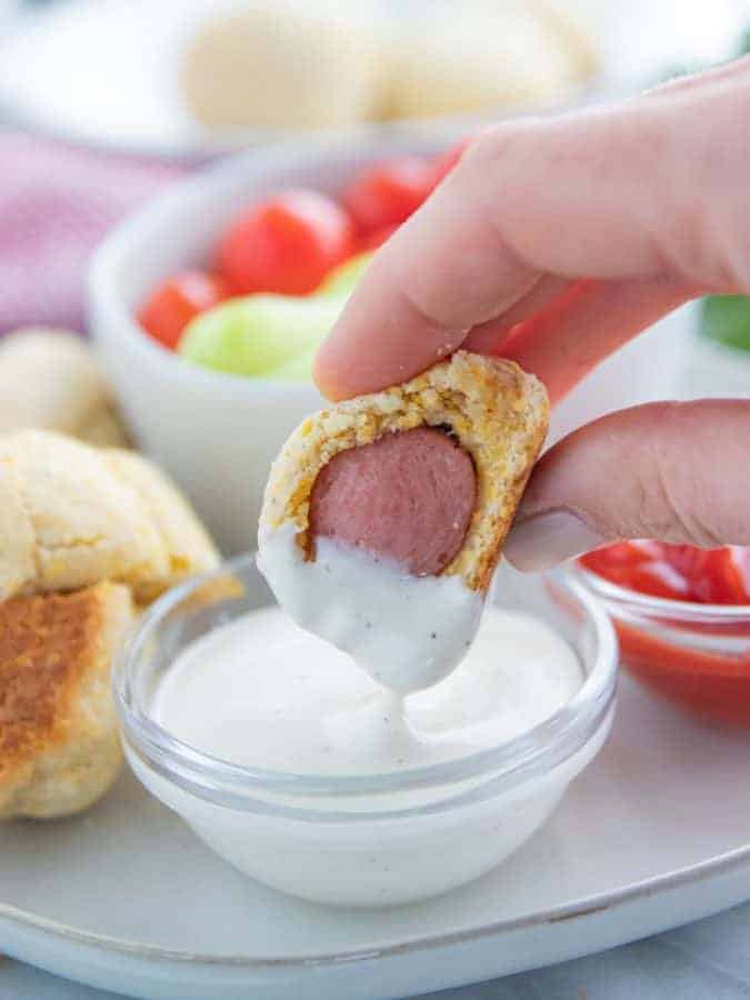 A close up of a corn dog dipped in ranch