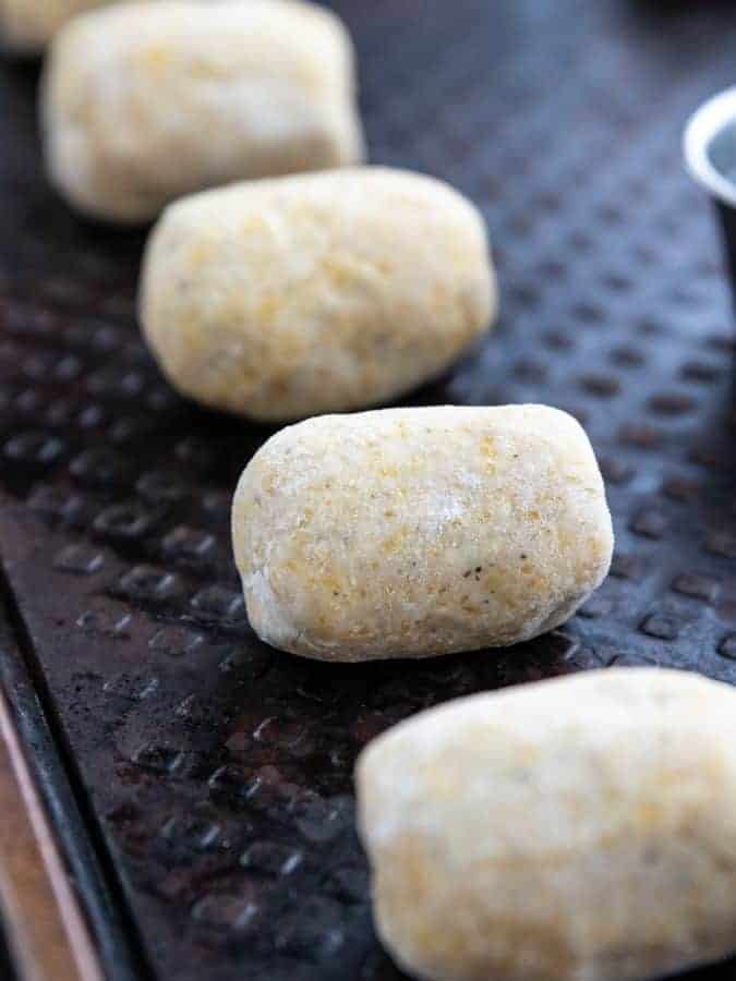 Mini Corn Dogs, a homemade baked corn dog recipe showing four uncooked mini corn dogs on a black baking sheet.