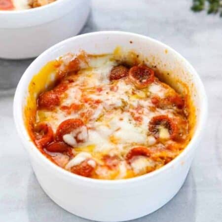 a microwave pizza is shown in a white ramekin with melted cheese and mini pepperonis.