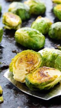 Roasted Brussels sprouts shown on a baking pan with a spatula taking some.