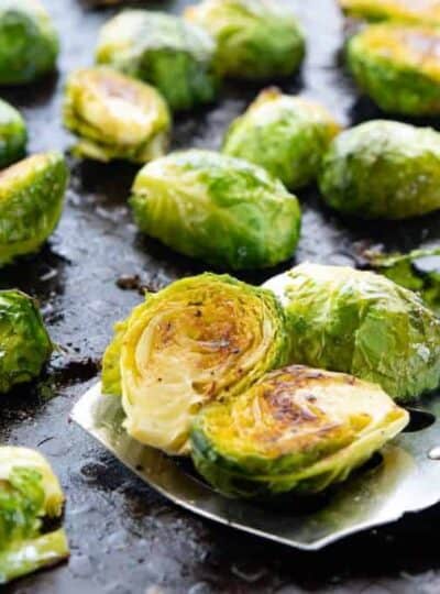 Roasted Brussels sprouts shown on a baking pan with a spatula taking some.