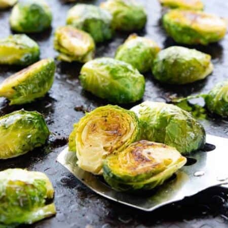 Roasted Brussels sprouts shown on a baking pan with a spatula taking some.