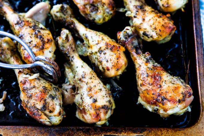 drumstick crockpot recipe, a flavorful chicken recipe showing chicken legs on a black baking dish with seasoning and a pair of tongs.