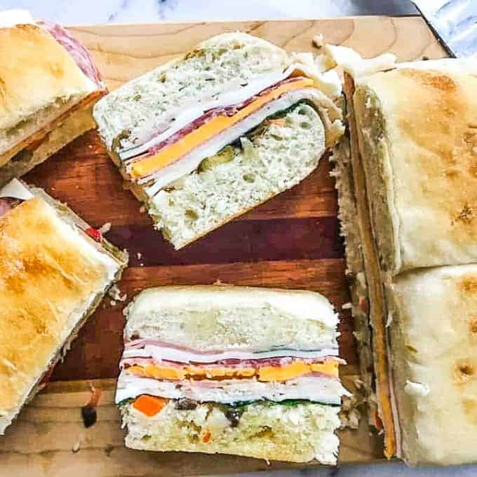 A piece of cake on a plate with a sandwich cut in half, with Muffuletta and Cheese