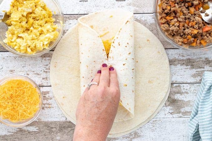 a hand folding a burrito 