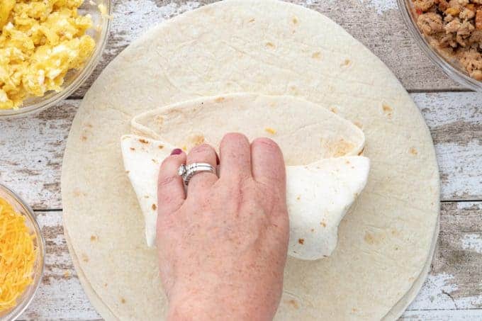 a hand folding a burrito shell