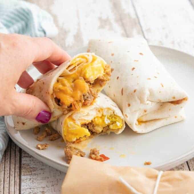 a hand holding a egg burrito sliced in half