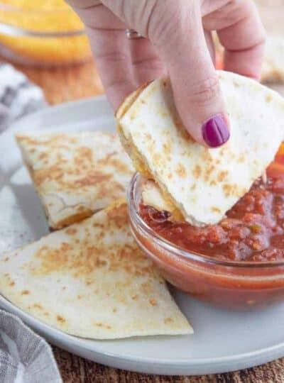 A person holding a piece of quesadilla diped in salsa