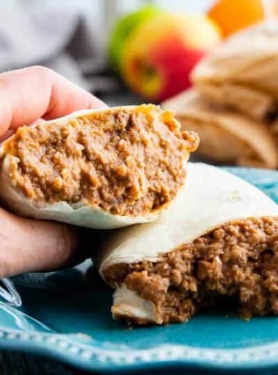 beef and beans wrapped in a tortilla cut in half with a hand holding one side on a blue plate.