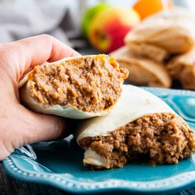 beef and beans wrapped in a tortilla cut in half with a hand holding one side.