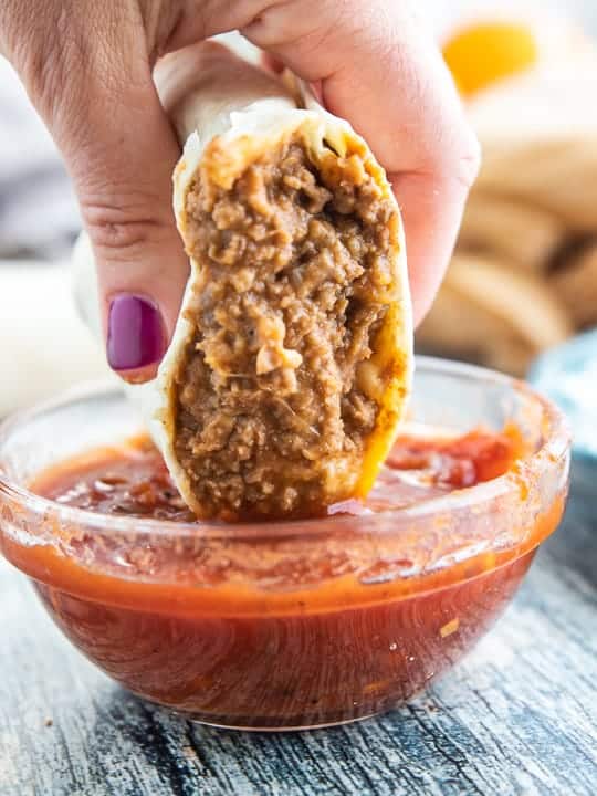 Beef and Bean Burrito cut in half and dipped in a glass bowl of salsa.
