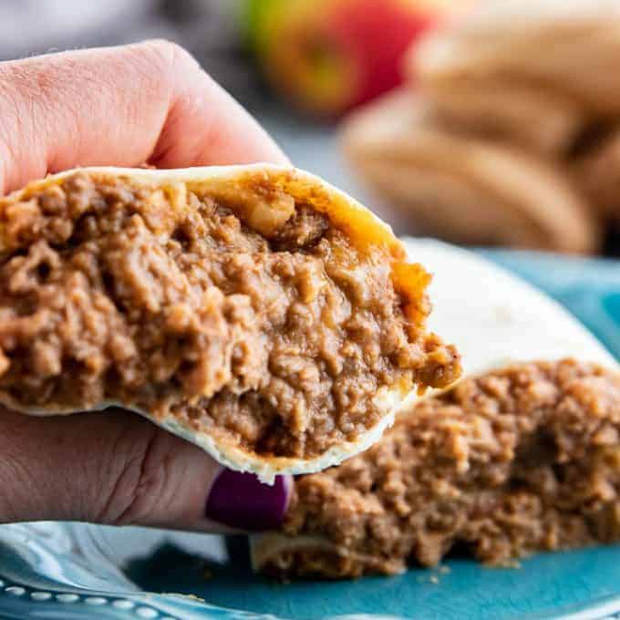 beef and beans wrapped in a tortilla cut in half with a hand holding one side.