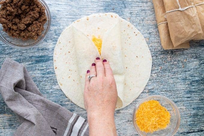 a person folding a tortillas ends in to fold.