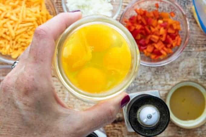 A person holding a mason jar with cracked eggs