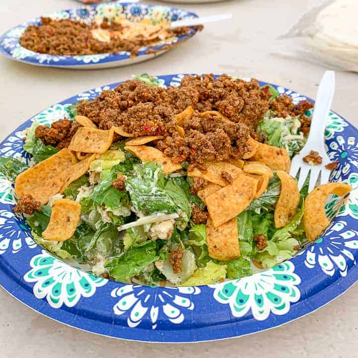 Camping Tacos shown on a paper plate with lettuce, Fritos, and taco meat.