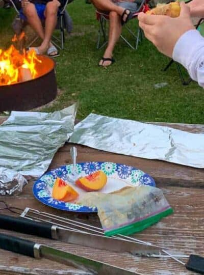 a paper plate with sliced peaches and a butter/sugar mixture is being prepared by a girl with tin foil.