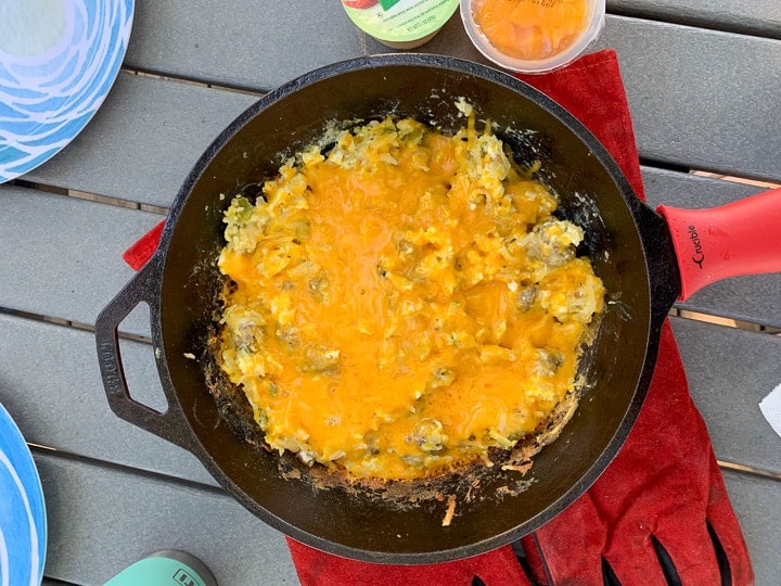 Cowboy Breakfast Skillet: Breakfast In Cast Iron Skillet shown on a picnic table. Egg and hash brown skillet is covered with cheese.