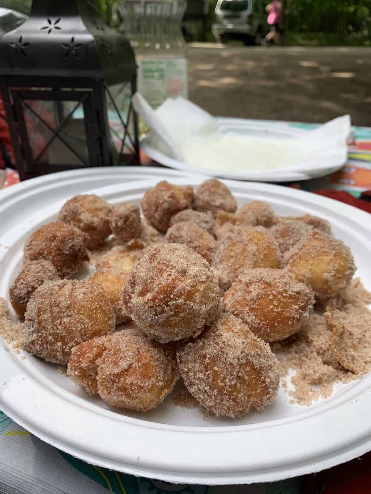 A paper plate loaded with homemade camping doughnuts covered in sugar and cinnamon.