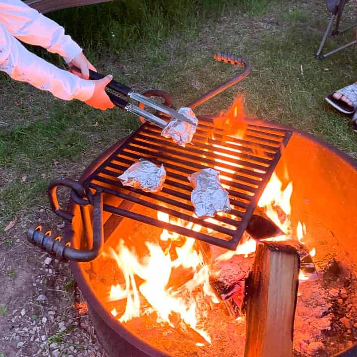 Foil garlic bread being heated over a campfire on a grate.