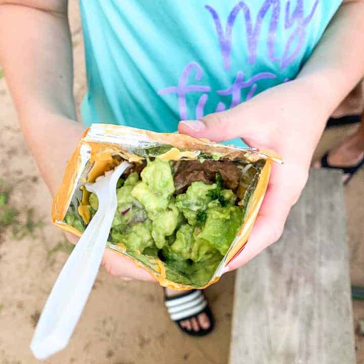 camping tacos shown in the hands of a tween girl with refried beans and guacamole in a Fritos bag with a fork 