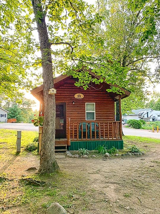 best camping in wisconsin at Evergreen campground in a standard cabin shown with trees surrounding the new looking small wooden cabin with a porch.