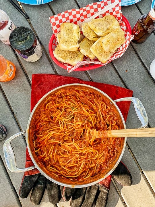 Easy camping garlic bread shown next to a pot of spaghetti in a stainless steel pot on a picnic table