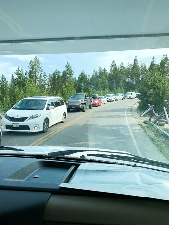 A view out of the rental rv showing a long line of cars waiting to get into a Parking lot in Yellowstone national park in July.