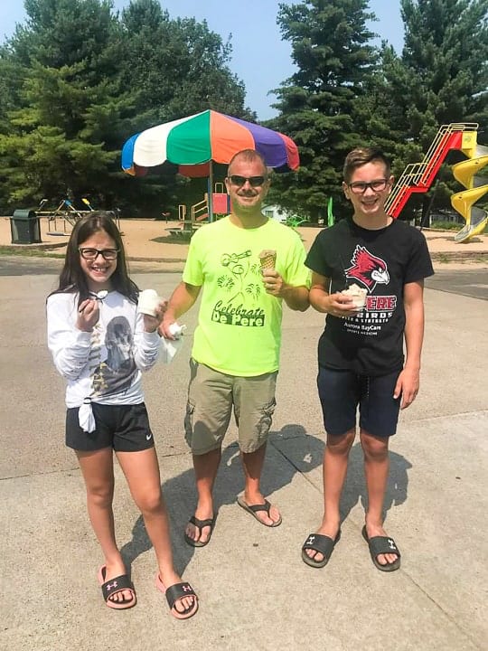 best camping in wisconsin includes ice cream! showing a girl, boy and their dad enjoying a cone by the park at evergreen campground in wi.