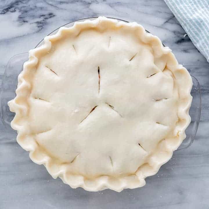 Slits cut into top of the creamy chicken pot pie shown on a marble surface.