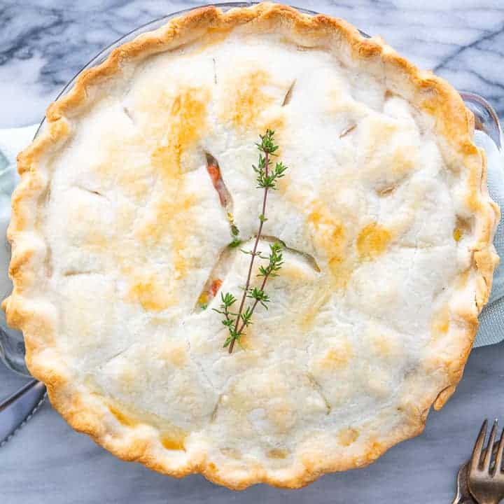 白い大理石の表面にパイの上にタイムの葉で焼いたクリーミーな簡単なチキンポットパイを示しています。