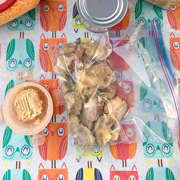 frozen roast potatoes shown in a ziplock bag next to homemade garlic butter on a picnic table with table cloth. 