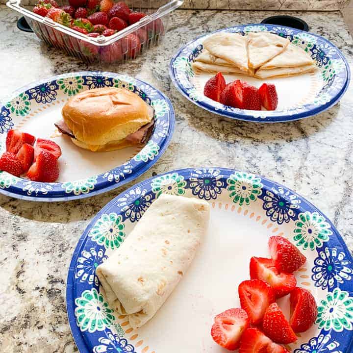 rv meals including a ham sandwich, quesadilla, and a burrito on paper plates with strawberries in an RV