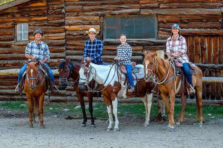 a family posing on horse back in plaid shirts and cowboy hats.