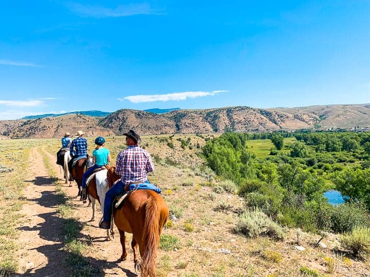 A family of four enjoying a horseback ride along a dirt path in Colorado headed back to the Colorado ranch to enjoy a homemade breakfast. 