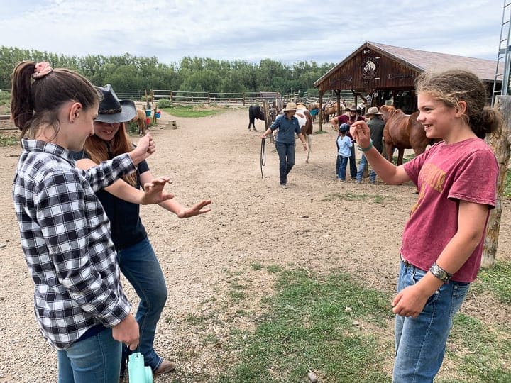 3 girls standing in the dirt outside a horse barn