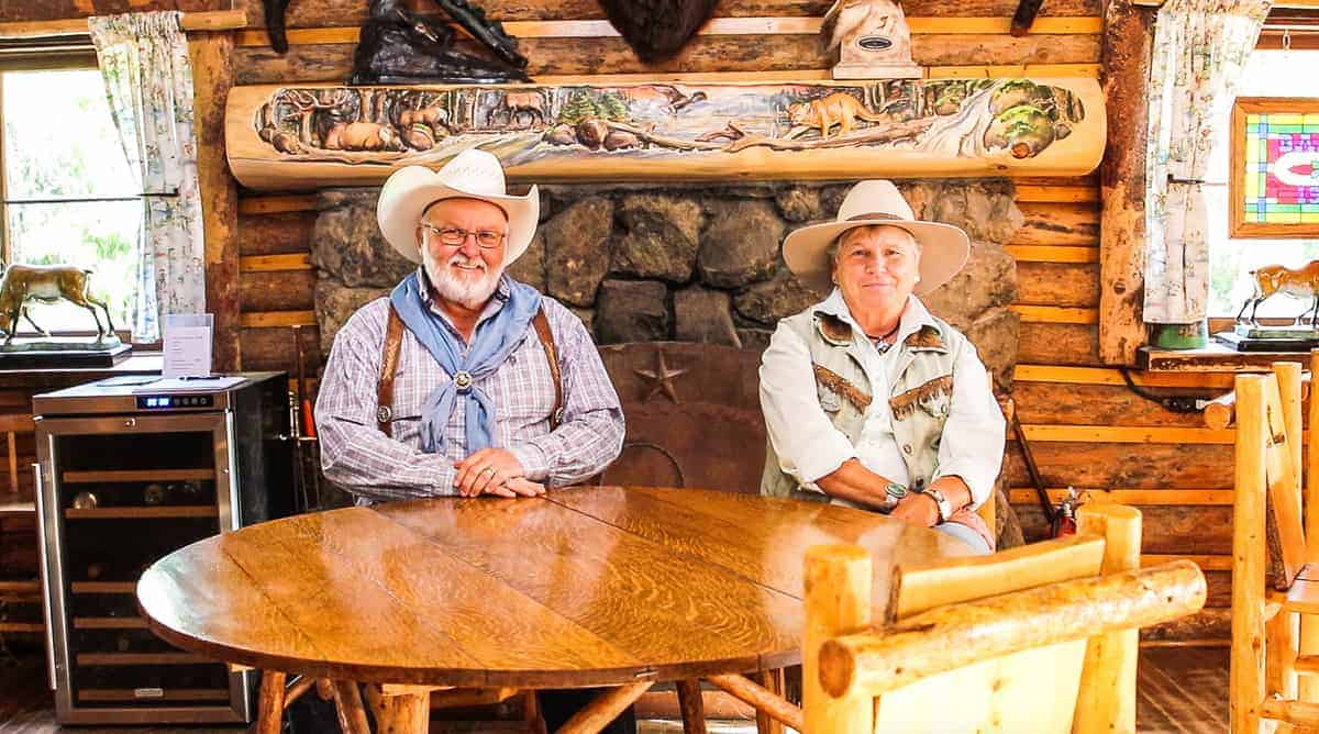 Bar Lazy J Guest Ranch Owners, Jerry & Cheri Helmicki being shown sitting an oak table with a fireplace behind them on a family dude ranch. 