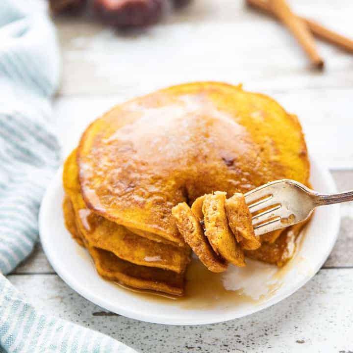 Healthy Pumpkin Pancakes, a pumpkin spice pancake recipe, showing a stack of pancakes on a white plate with a fork.