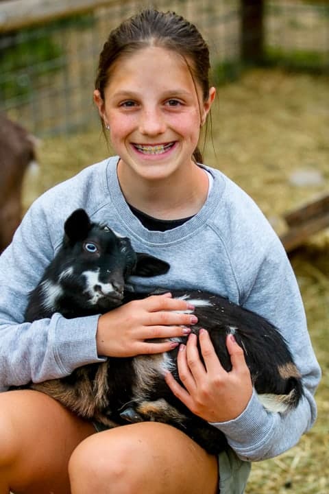 family ranch vacation showing a girl holding black and white baby goat.