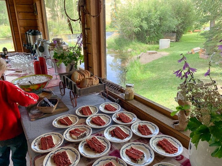 Slices of red velvet cake plated on white plates set on a long table with other desserts.