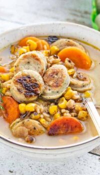 Chicken sausage soup with carrots, corn and rice shown with a spoon in a white bowl.