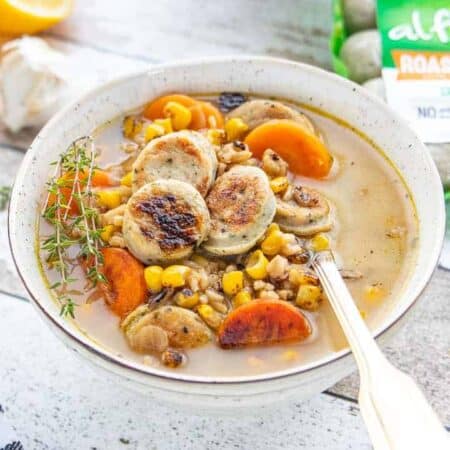 Chicken sausage soup with carrots, corn and rice shown with a spoon in a white bowl.