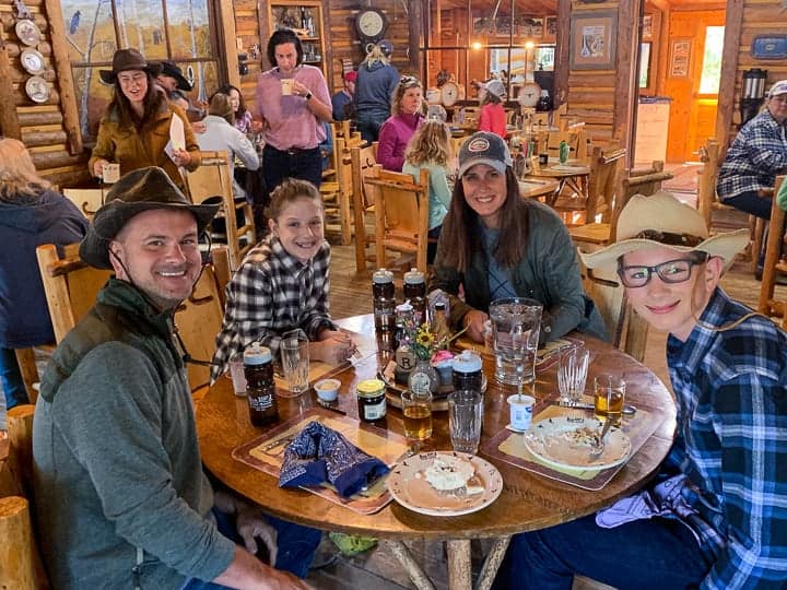 A family of four being shown sitting at a table eating a meal while enjoying an all-inclusive dude ranch vacation in Colorado.