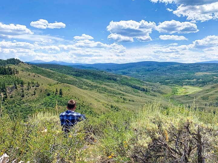 A teen boy sitting on a mountain in Colorado with mountains in the distance.