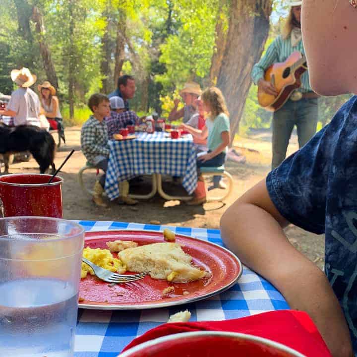 Breakfast in the woods eaten on picnic tables with a cowboy playing the guitar.