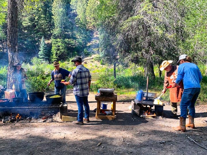 A man and a woman getting their plates filled by staff in the woods at a clearing for a breakfast site.