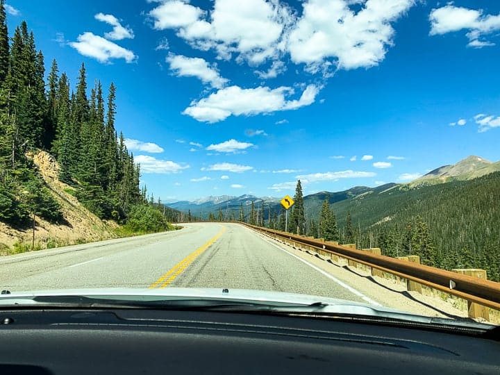 A car being shown driving down a highway from a passenger's view with the Colorado scenery surrounding the car headed to a family dude ranch.