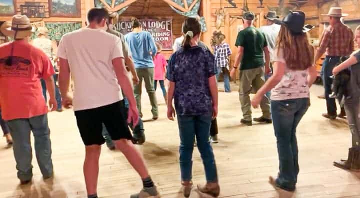 A large group of adults and teens line dancing in an activity barn.
