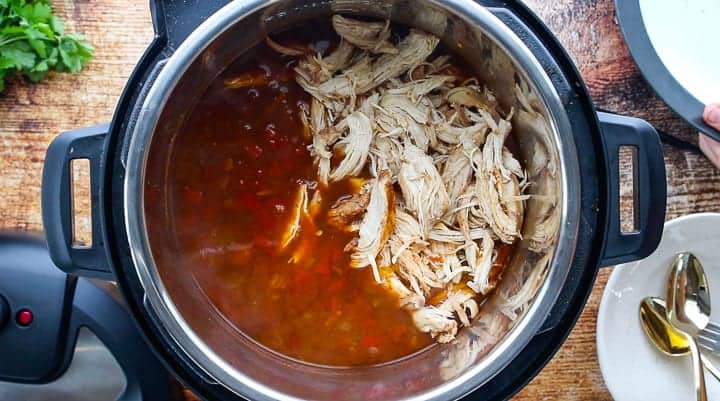 Instant Pot Chicken Tortilla Soup, an instant pot tortilla soup recipe, showing the soup in the pot with the chicken being shredded.